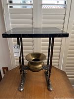 Front view of vintage small wrought iron table with black marble top and claw paw feet, brass spittoon placed in center opening below tabletop.