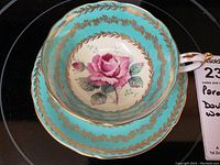 Top view of cup and saucer showing detailed pink cabbage rose on turquoise background with gold floral garland design