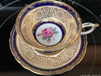 Top view showing cup and saucer with detailed cabbage rose centre and ornate gold decoration with cobalt blue bands.