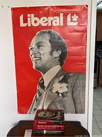 Full view of large political poster with image of Pierre Elliott Trudeau in suit and tie, with 'Liberal' text and logo on red background. Poster shows pin holes in the corners.