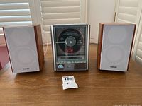 Front view of the complete stereo system with the CD player in the center and the two speakers on either side on a wooden table.