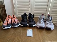 Front view of three pairs of women's running shoes, coral Adidas, black Nike, and pink Nike, displayed on wooden table.