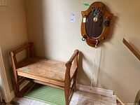 Wood hall bench and wood frame mirror mounted on wall, with keychains hanging and green boot mat under bench.
