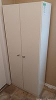 Closed white cabinet with two doors and metal handles, tall and narrow design.