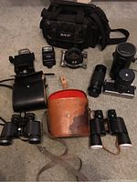 Overview of the lot showing Minolta XG-M camera with Ozawa lens, Sigma zoom lens, flashes, binoculars, and carrying bag