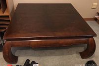 Front view of square wooden coffee table showcasing surface scratches and curved legs.