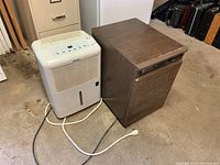 Two dehumidifiers: white Danby with visible control panel and water tank, and brown Mastercraft with wood-like finish side by side on floor.