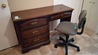 Full view of dark wood desk with four drawers and grey office chair beside it on tiled floor.