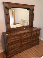 Large wooden dresser with nine drawers and large framed rectangular mirror hutch attached, showing carved wood details and metal pulls.