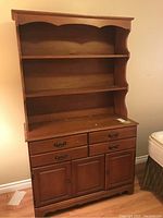 Photo of wood veneer dresser with 4 drawers, metal pulls, and 2 doors below, placed against a beige wall with part of a bed visible.