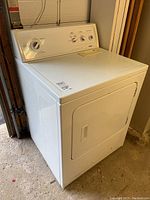 White Kenmore front loading dryer showing control panel and front door from an angle in garage.