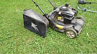 Side view of black yard mower with attached rear grass catcher bag on grass surface