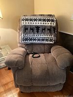 Front view of the brown corduroy lift recliner with a patterned blanket draped over the backrest and the remote control resting on the seat cushion.