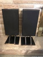 Pair of Paradigm speakers standing on black speaker stands, against a brick wall background