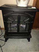 Front view of black Muskoka electric fireplace showing molded plastic frame and double front doors with glass panes.
