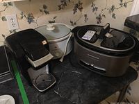 Full view of Keurig coffee maker and two slow cookers on black marbled countertop
