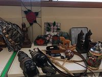 Photo displaying stained glass pieces, Indigenous figures, carved wood bookends, leather items, ceramic stein, wall clock and other small objects on a table.