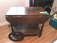 Side view of wood tea cart with extension leaves folded down showing large spoked wheel and caster wheel.