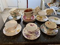 View of all seven vintage teacups and saucers laid out on countertop, showing floral patterns and various colors.
