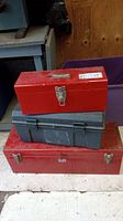 Three tool boxes stacked; small red metal box on top, gray plastic box in middle and large red metal box on bottom.