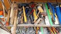 Photo showing an assortment of wooden handled hammers, mallets, and other hand tools arranged on a shelf.