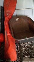Photo showing rusty metal wheelbarrow bucket and orange tarp rolled beside it