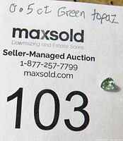Photo of the loose green topaz gemstone on auction paper showing '0.5 ct Green topaz'