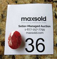 Front view of the oval faceted ruby gemstone placed on auction card with lot number 36