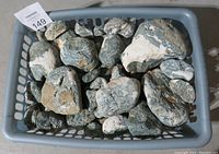 Tray containing approximately 23 Dallasite volcanic breccia rocks in grey basket, showing size and variety.