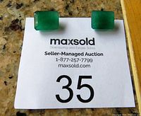Two rectangular faceted green jade stones placed on a paper with auction info showing lot number 35.
