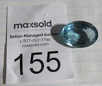 Aquamarine gemstone placed next to auction tag number 155 on a paper background.