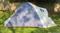 Side view of blue, gray and orange Coleman Excursion tent set up on grass, showing tent profile and Coleman logo.