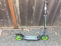 Full side view of green and gray adult scooter with green wheels on gravel ground near wooden fence