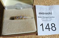 Close up of gold tone ring with five clear cubic zirconia stones set in a row, displayed in a box upholstery.