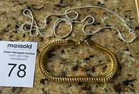 Two chains displayed on a granite countertop: gold tone thick chain bracelet and silver tone thin chain necklace.