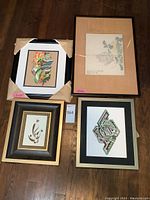 Four framed art pieces laid on the floor: includes abstract, Asian print, calligraphy and lithograph art.