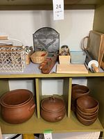 Wooden and ceramic pots on lower shelves, wooden bowls on the right side, multiple kitchen accessories on the shelf above including a rolling pin and flatware.