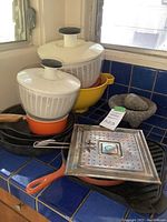 Overview showing salad spinners, yellow bowl, granite mortar, orange-handled skillet with rack and cast iron pan beneath