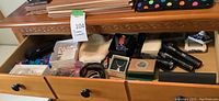 Open wooden drawer containing assorted jewelry boxes, knitted mitt, wristwatch, comb, and flashlights.