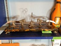 Wide view of seahorse cheese spreaders on tortoiseshell base with Veuve Clicquot champagne bottle decor in background
