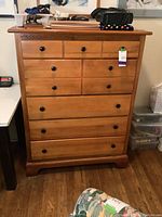 Front view of a solid wood dresser with seven drawers and black round knobs, decorative carved trim below top surface.