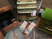 Photo showing fishing tackle storage boxes with various fishing equipment including hooks, sinkers, and cork floats, along with unopened packs of fishing hooks