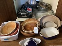 Overview of lot showing wooden bowls, plastic bowls, ceramic bakeware, metal pans, stacked cookware items