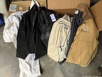 Four men’s jackets in open box: black leather coat, beige North Face jacket, tan Carhartt coat, partial white garment visible