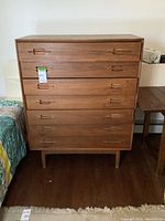 Front view of tall teak dresser showing five recessed-handle drawers and cylindrical legs.