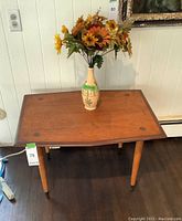 Front angled view of table top and legs with vase holding artificial flowers