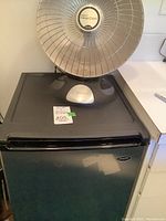 Front view of Presto HeatDish heater sitting on top of Sanyo mini fridge showing the heater control panel and metal mesh reflector.