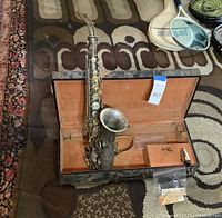 Full view of the saxophone in its open hard case with orange velvet lining.