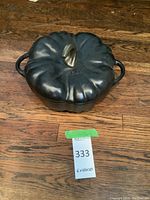Top view of closed black cast iron Dutch oven shaped like a pumpkin with bronze stem knob and Staub branding on lid.