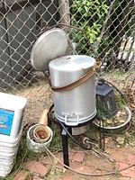 Full view of the aluminum still on a black metal stand with burner underneath, exterior showing signs of rust on the clamp.